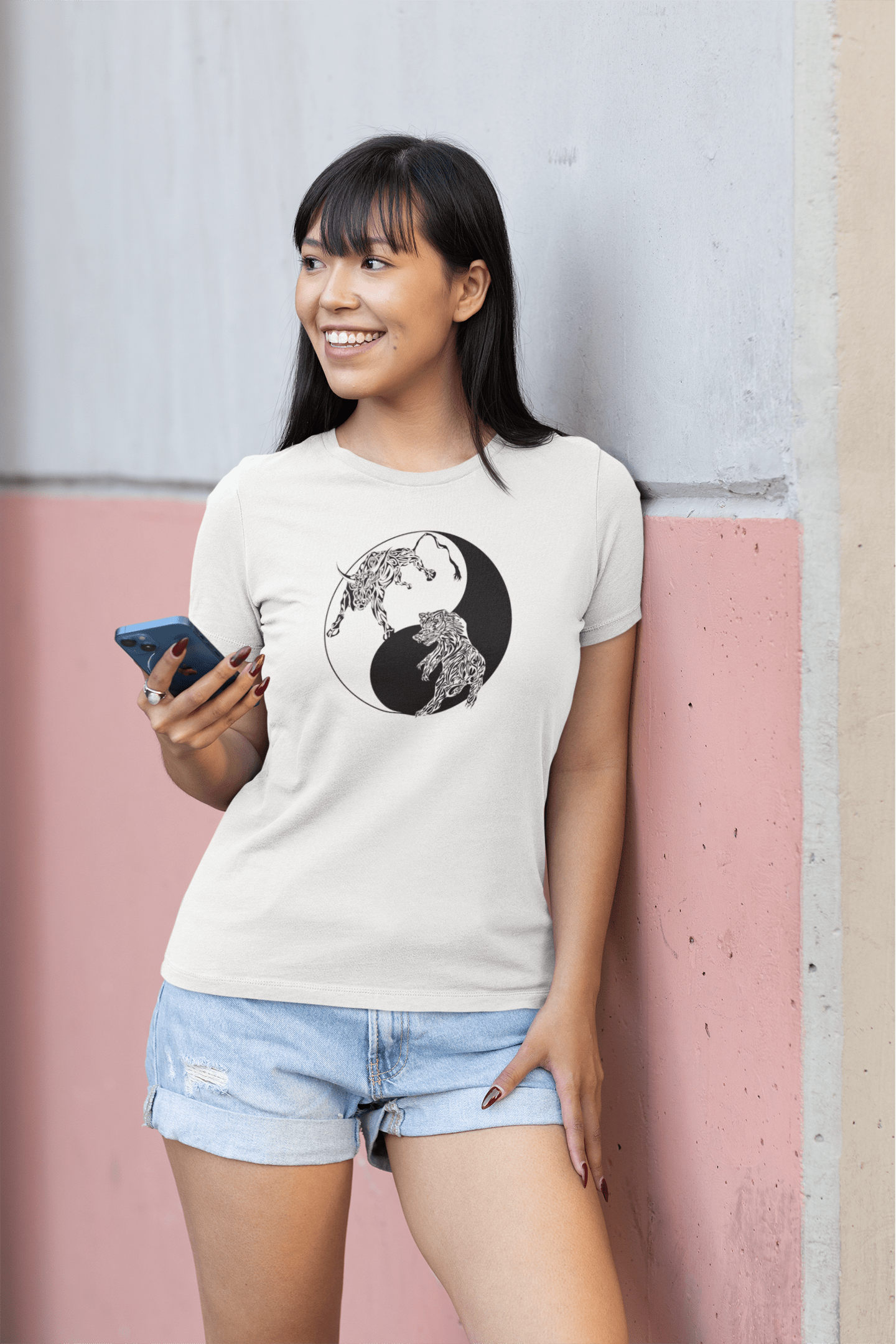 A woman wearing our Bullish/Bearish - Yin Yang - Tribal design, without text, on a white t-shirt while leaning up against a pink and white wall.