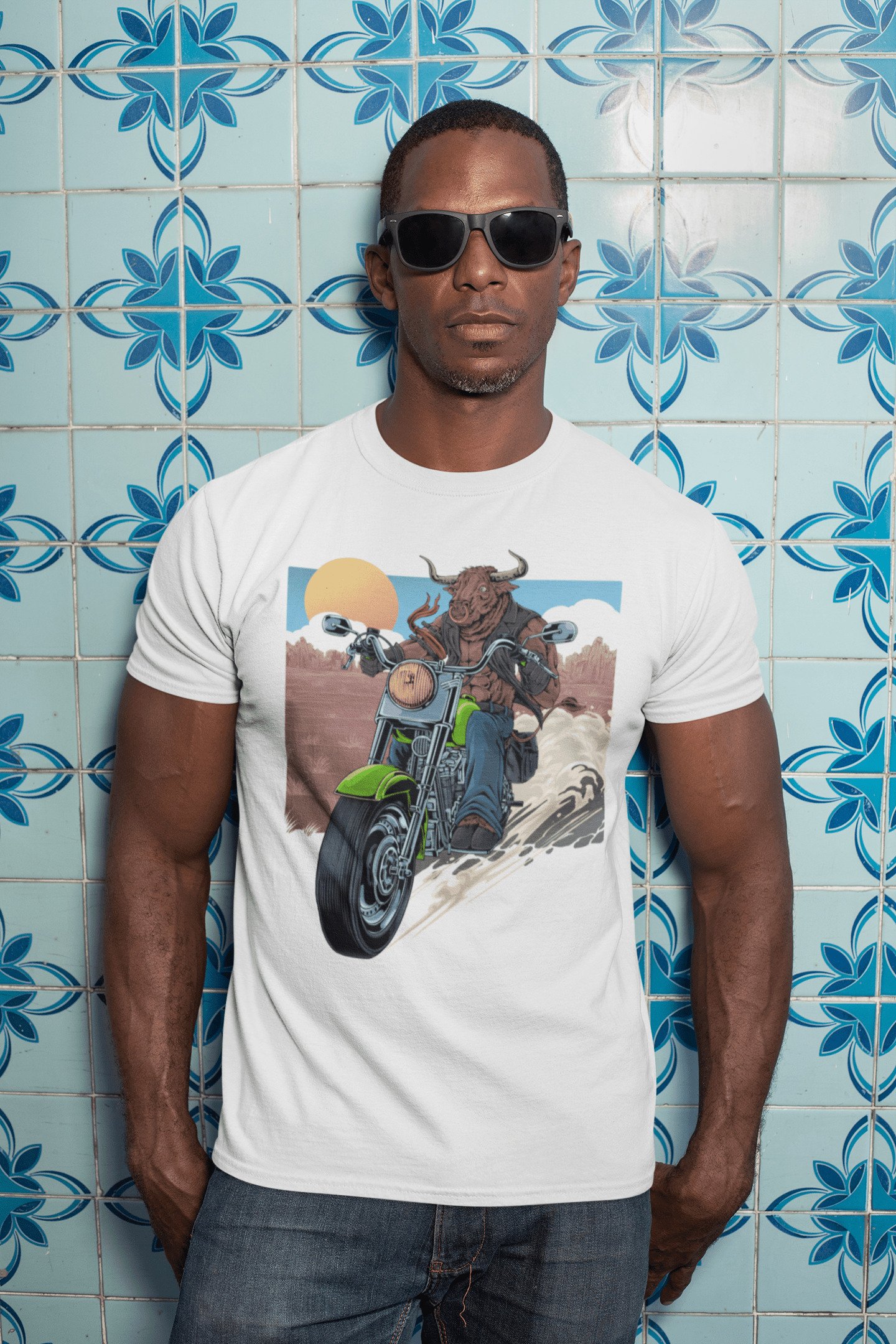 A man with sunglasses against a blue tiling wearing a white t-shirt with a Bull riding on a motorcycle.